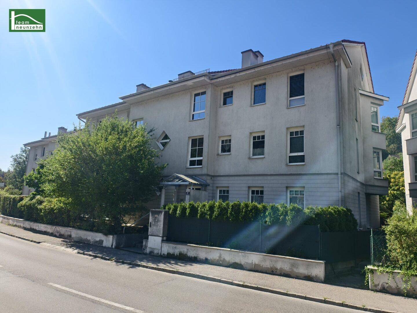 Ansicht des Mehrfamilienhauses von der Straße mit gepflegter Fassade und umgebender Hecke.