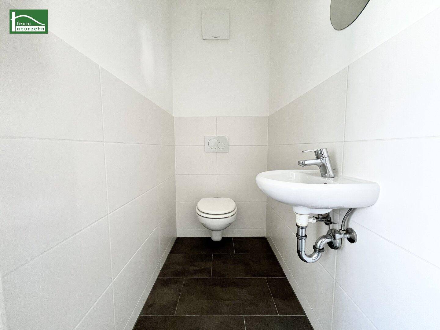 Modernes Gäste-WC mit Wand-WC, kleinem Waschbecken und dunklen Bodenfliesen.