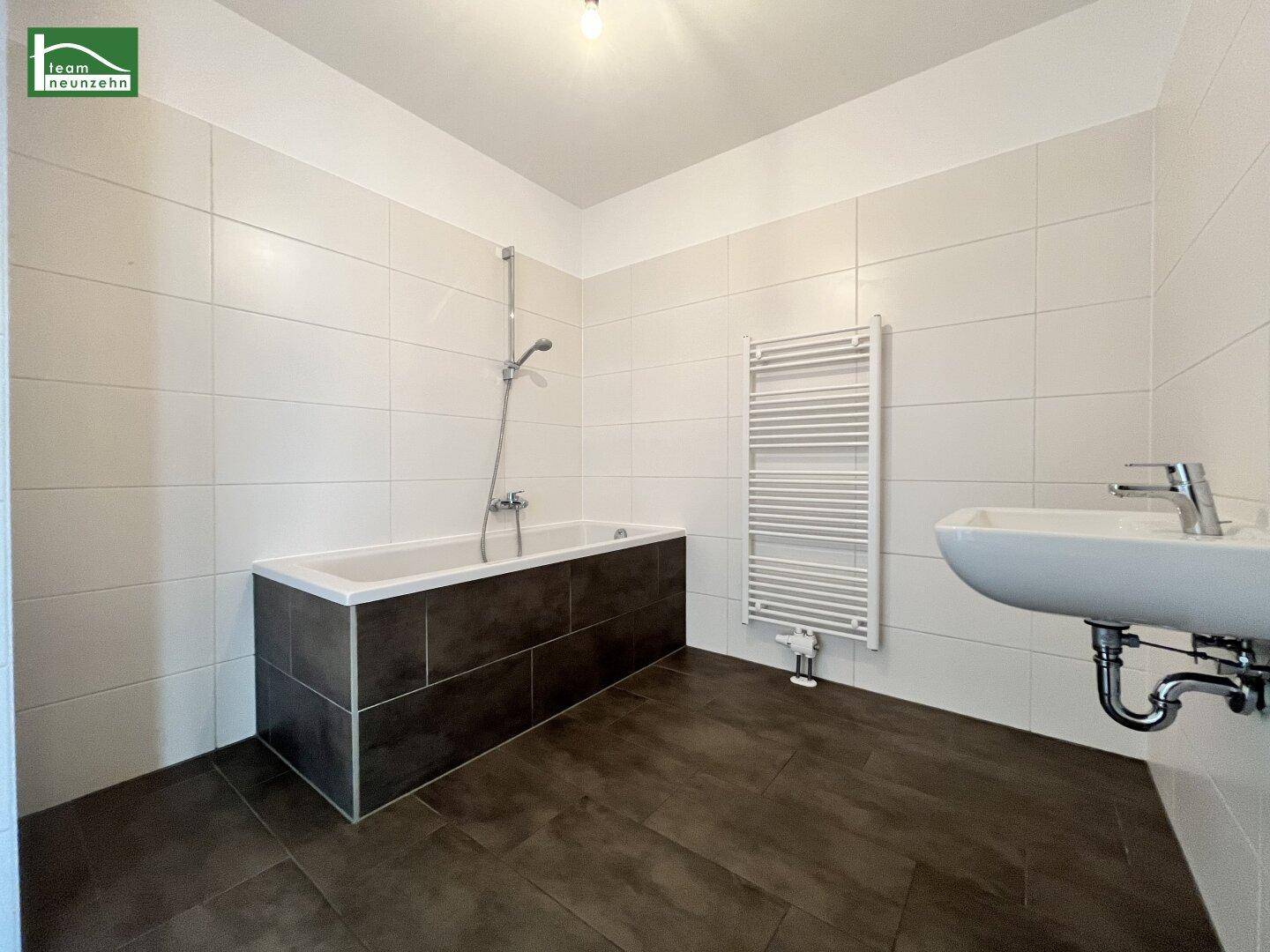 Modernes Badezimmer mit Badewanne, Waschbecken, beheiztem Handtuchhalter und dunklen Fliesen.