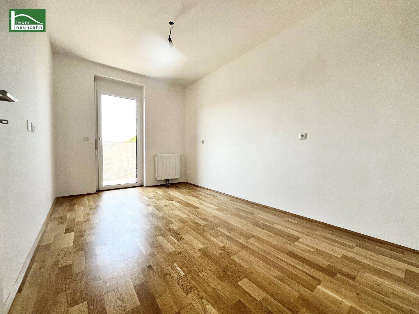 Leeres Schlafzimmer mit Parkettboden und Balkonzugang, bereit zur individuellen Einrichtung.