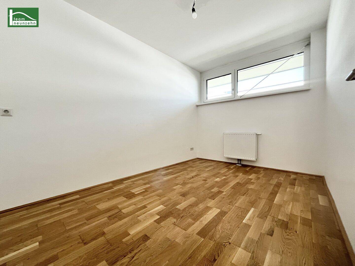 Leeres Schlafzimmer mit Parkettboden und großem Fenster, bereit zur individuellen Gestaltung.