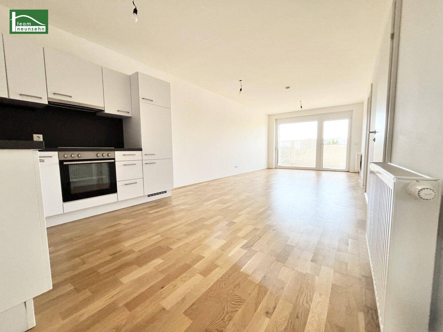 Offener Wohnbereich mit integrierter Küche, Parkettboden und Zugang zum Balkon.