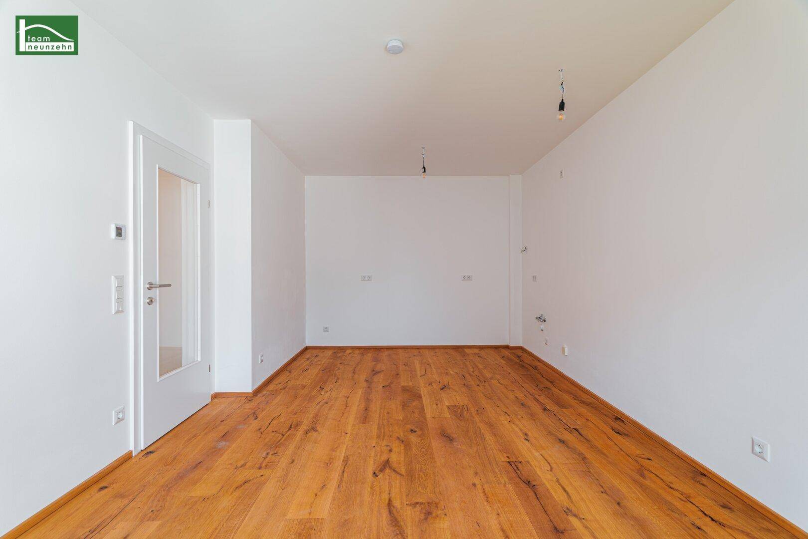 Leeres, helles Zimmer mit Holzboden und einer Tür mit Glaseinsatz, bereit zur individuellen Gestaltung.