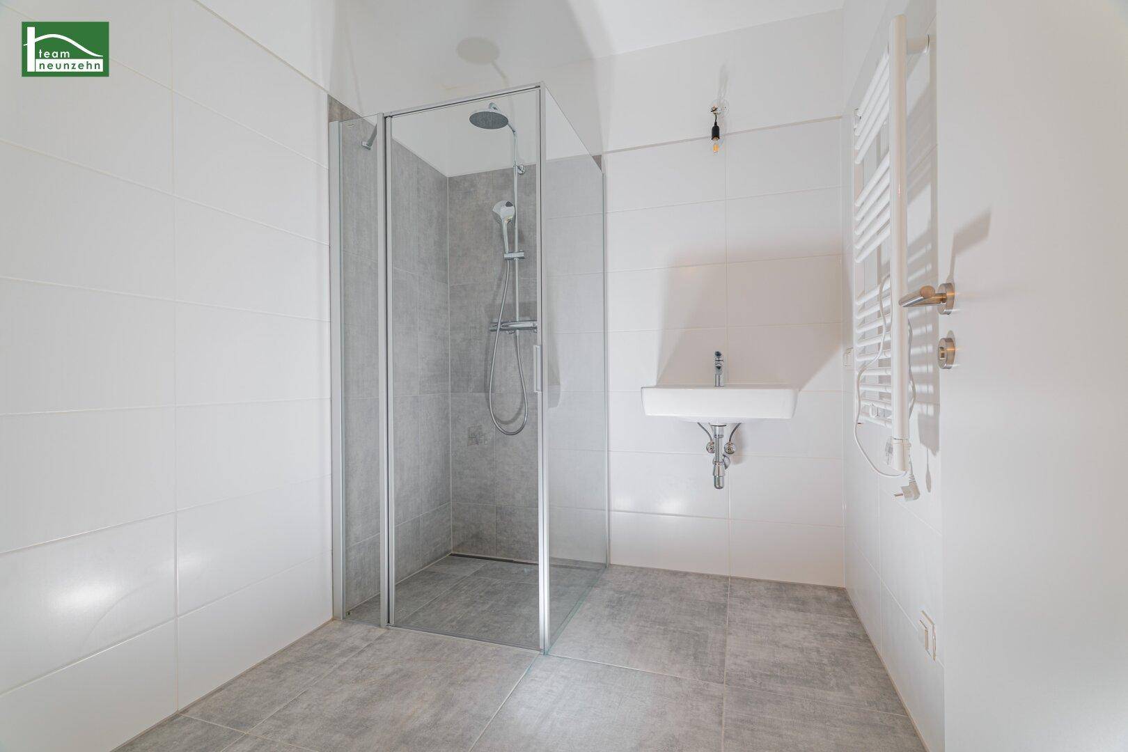 Modernes Badezimmer mit großer Duschkabine, Waschbecken und beheiztem Handtuchhalter.