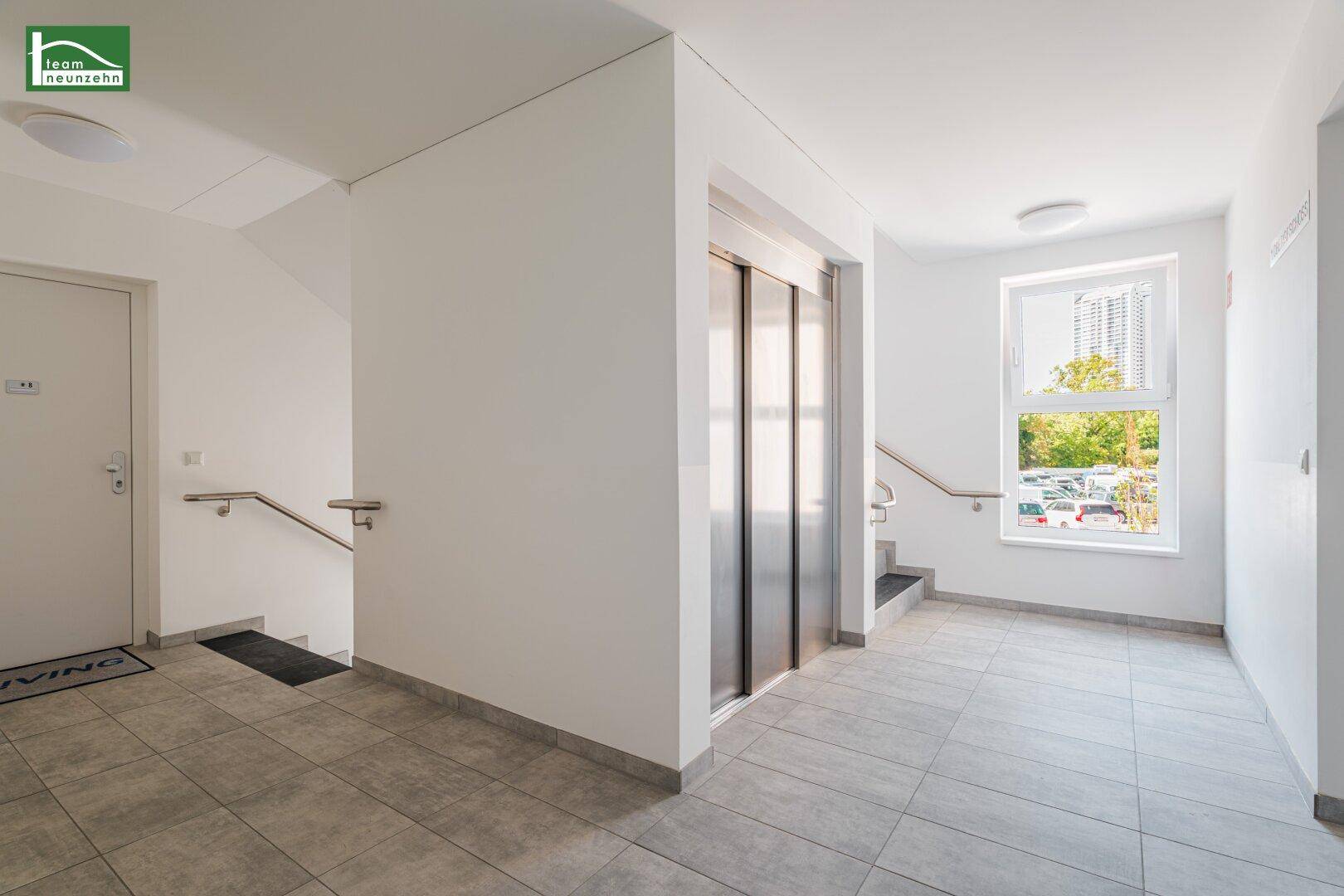 Heller Eingangsbereich mit Aufzug, Treppe und Fliesenboden, barrierefrei zugänglich.