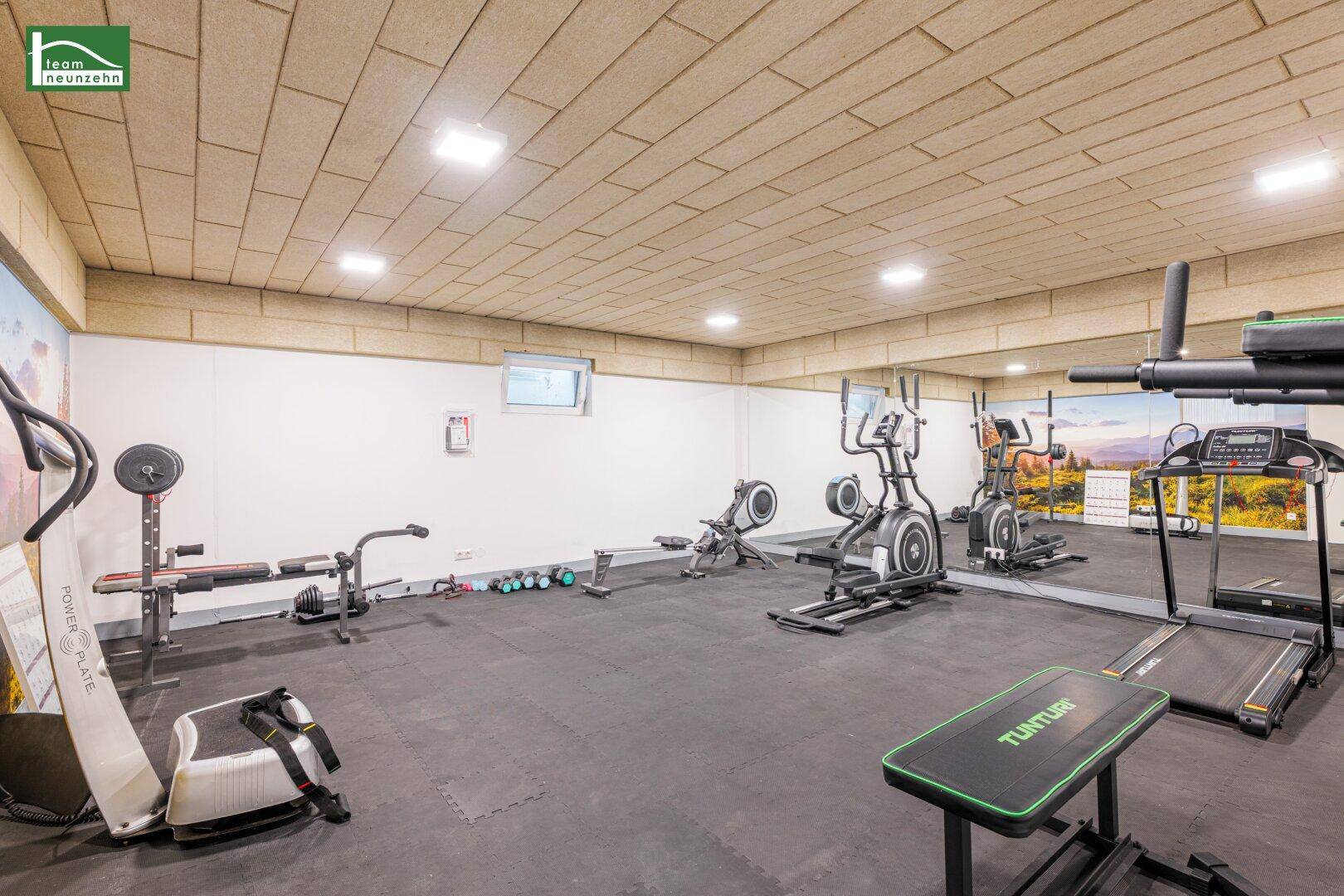 Gut ausgestatteter Fitnessraum mit verschiedenen Trainingsgeräten und Spiegelflächen.