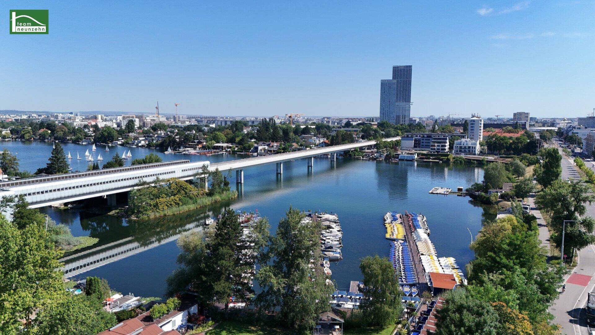 Weitläufiger Blick über einen See mit Brücke, Booten und der Stadt im Hintergrund.
