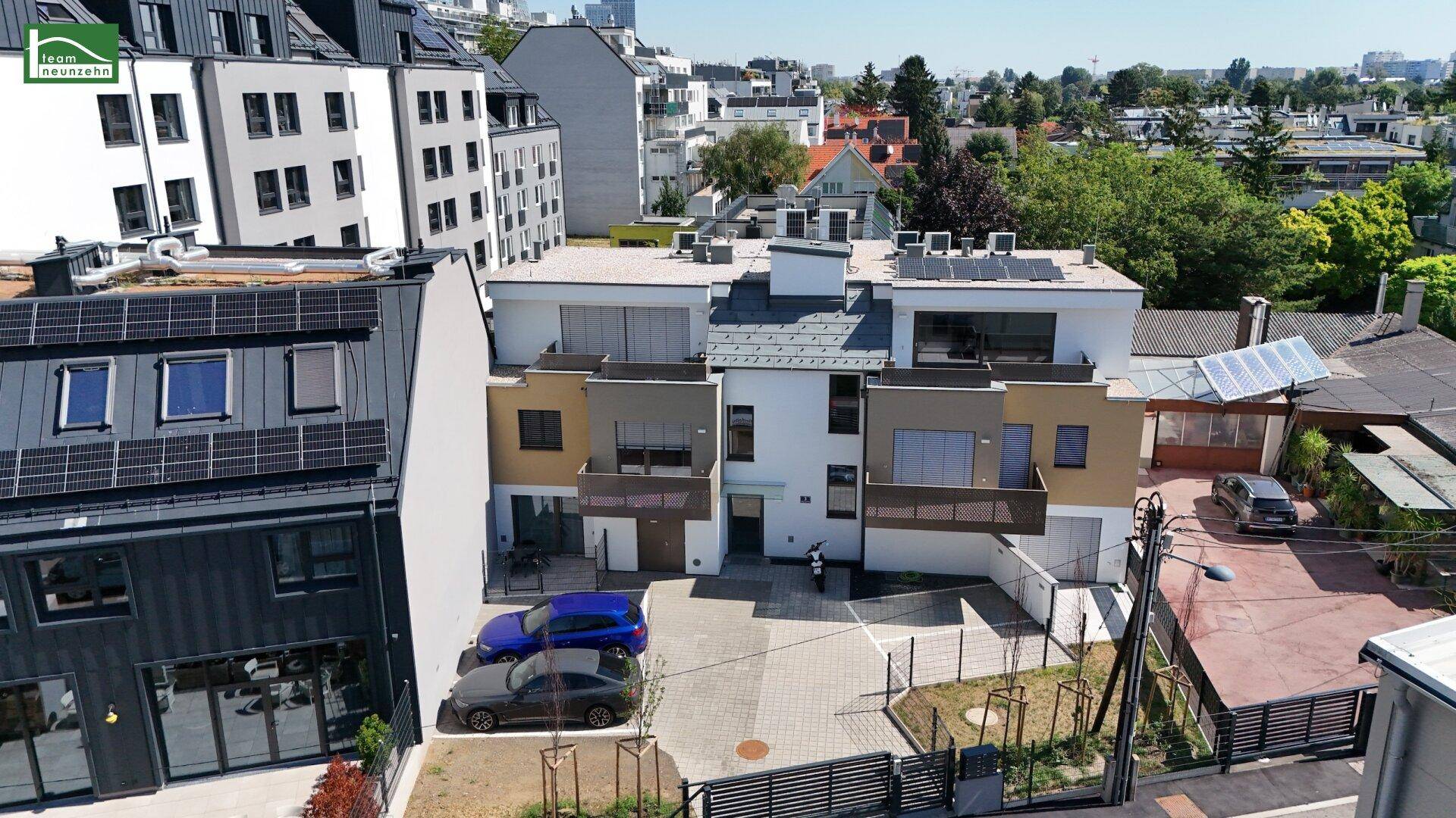 Luftaufnahme der Reihenhäuser mit Solaranlagen auf den Dächern und umliegender Stadtlandschaft.