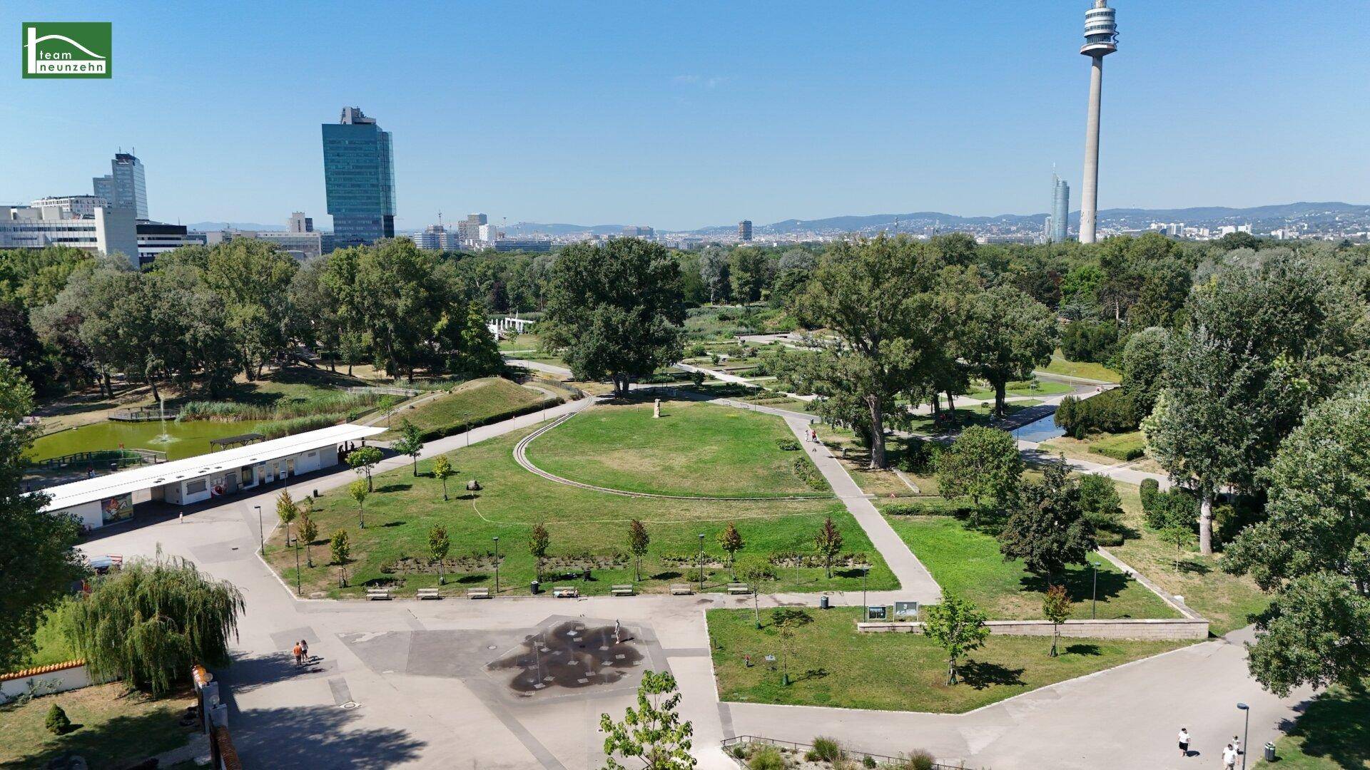 Luftaufnahme eines grünen Stadtparks mit Spazierwegen und dem Fernsehturm im Hintergrund.