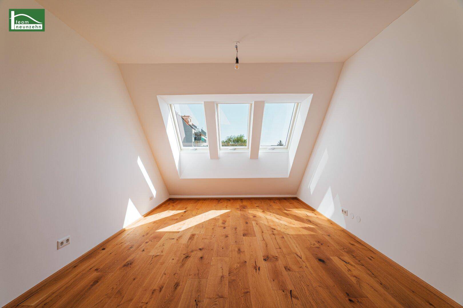 Helles Dachzimmer mit Holzboden und drei Dachfenstern für viel Tageslicht.