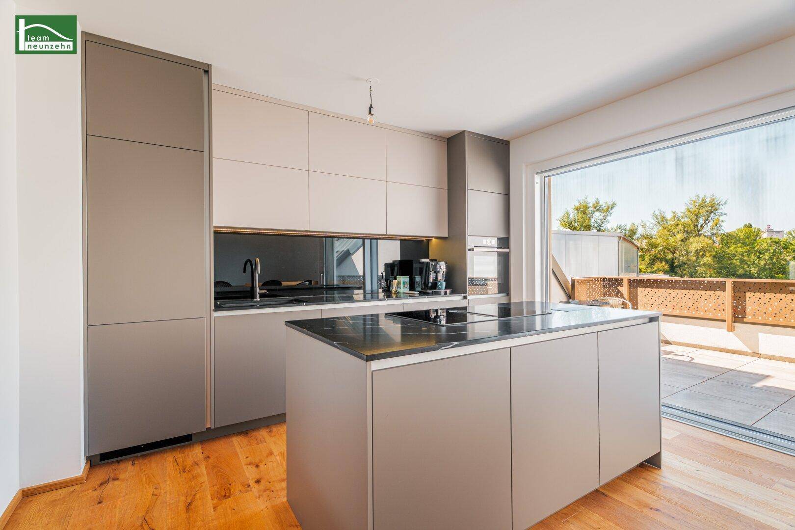 Moderne Küche mit Kücheninsel, dunkler Arbeitsplatte und direktem Zugang zur sonnigen Terrasse.