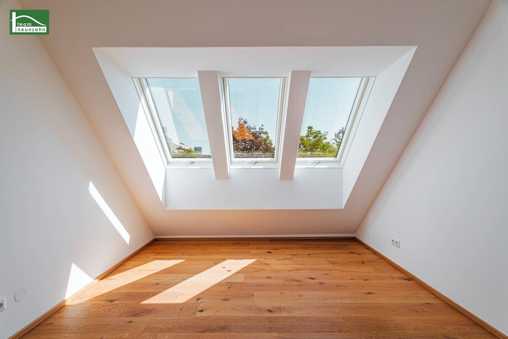 Dachzimmer mit schrägen Wänden und drei großen Dachfenstern für viel Helligkeit.