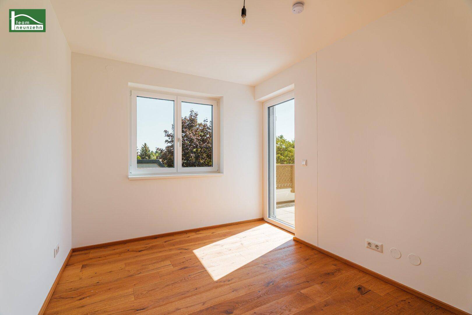 Kleinerer Raum mit Holzboden, Fenster und Zugang zu einem Außenbereich, sonnig.