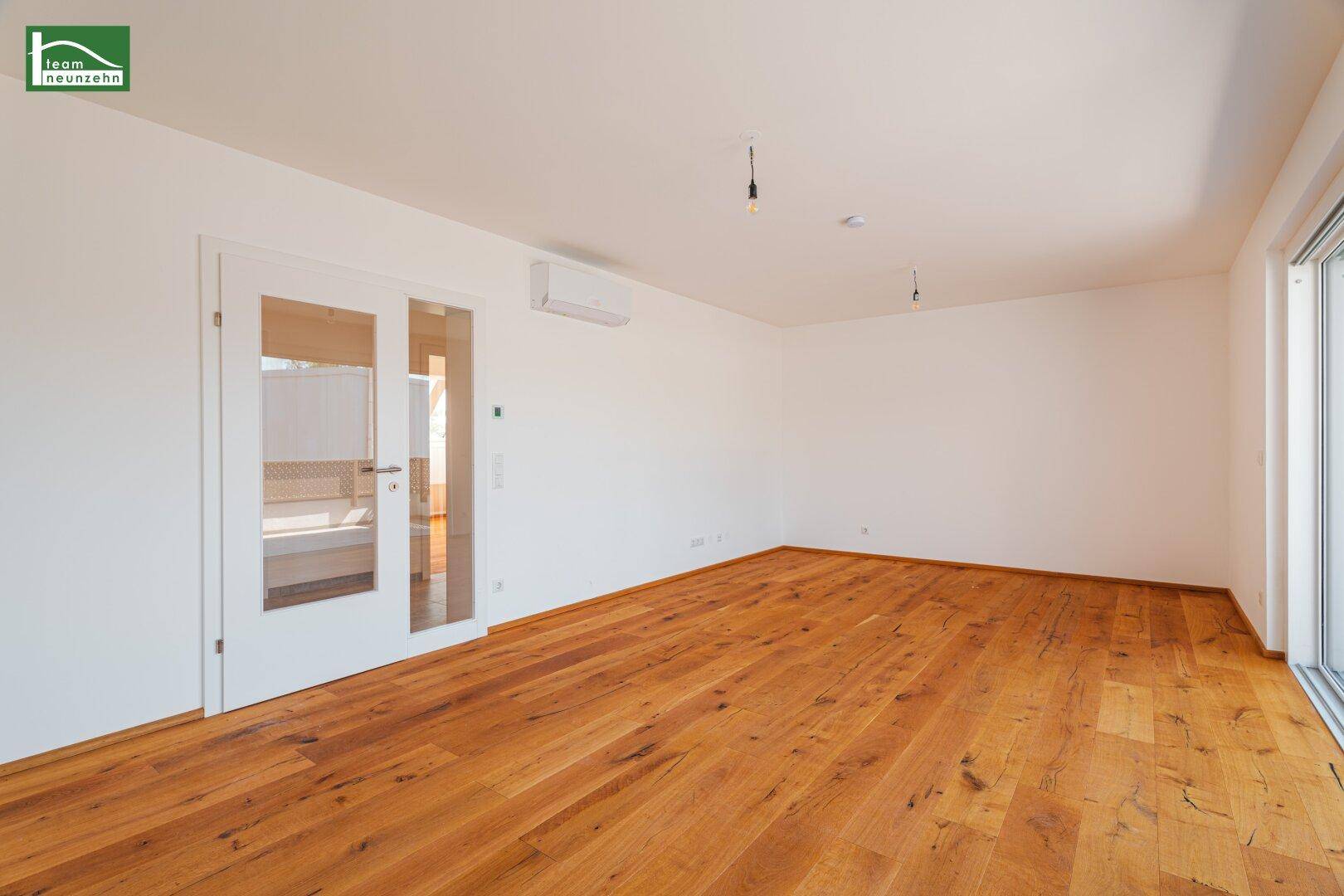 Heller Wohnbereich mit Holzboden, weißen Wänden und einer Tür mit Glaseinsätzen.