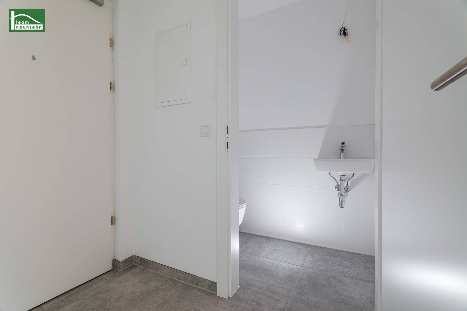 Modernes Gäste-WC mit Fliesenboden, wandmontiertem Waschbecken und Toilette.