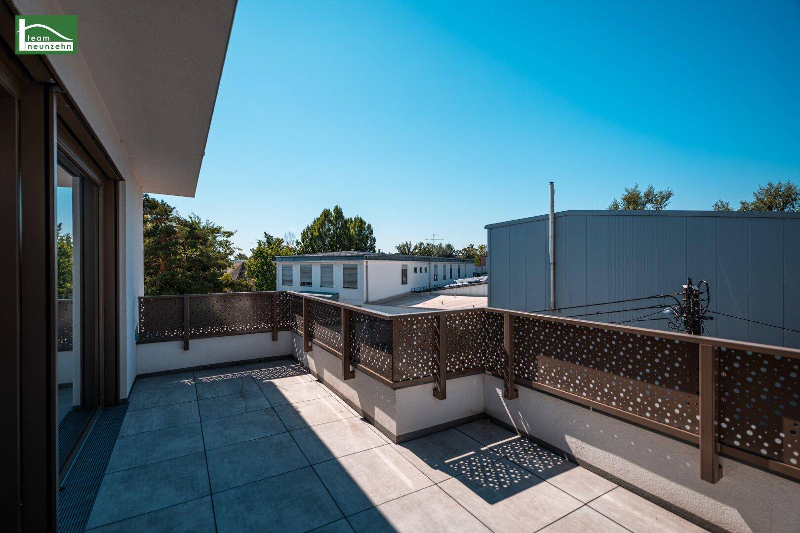 Sonnige Terrasse mit Fliesenboden und Blick auf die umliegenden Gebäude und Bäume.