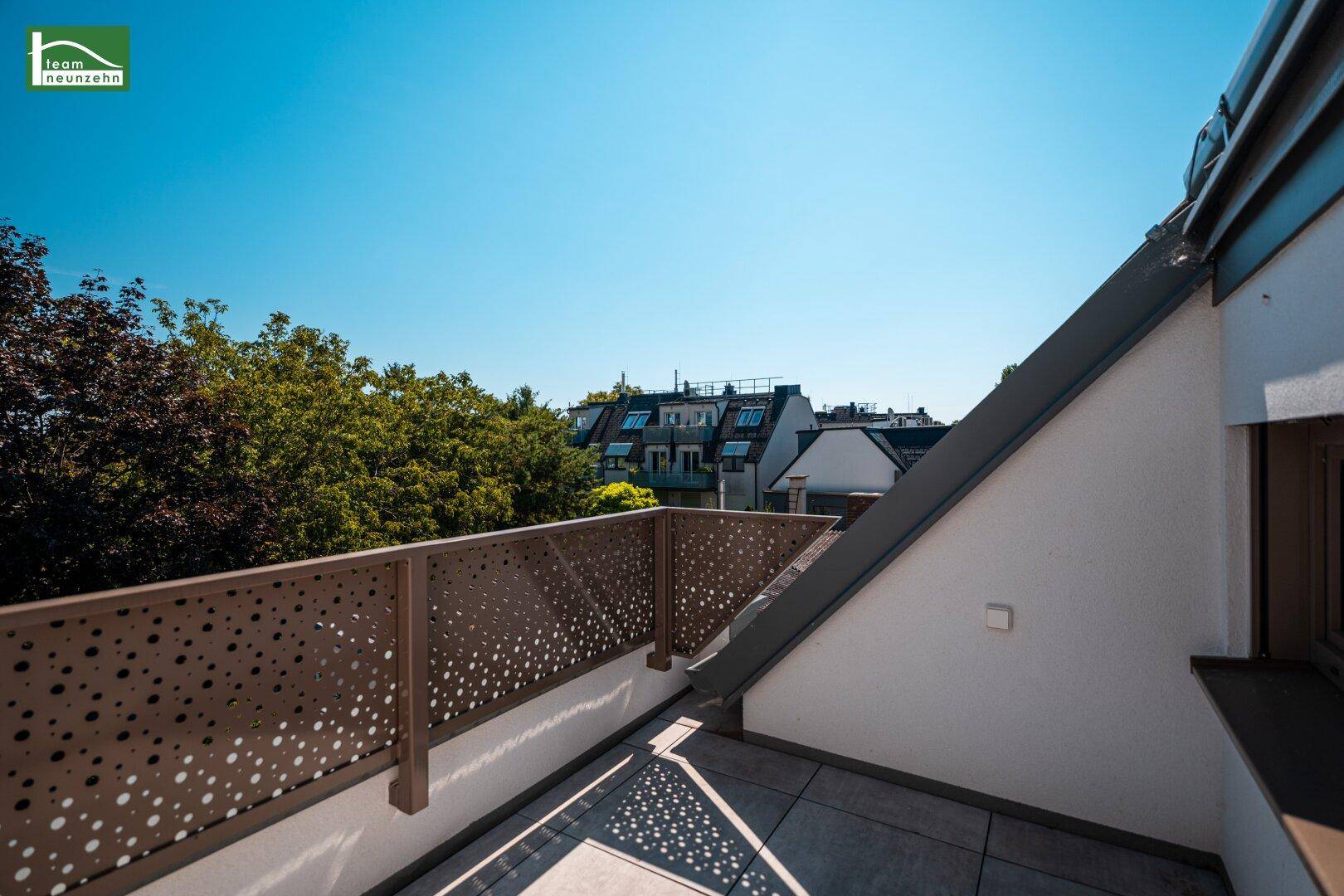 Sonnige Terrasse mit moderner Brüstung und Blick auf die Dächer und Bäume.