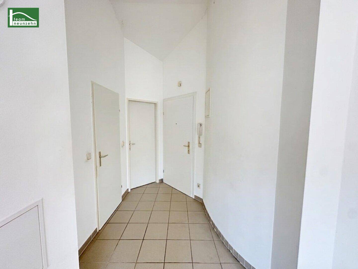 Schmaler Flur mit Fliesenboden und mehreren Türen, der zu verschiedenen Räumen führt.