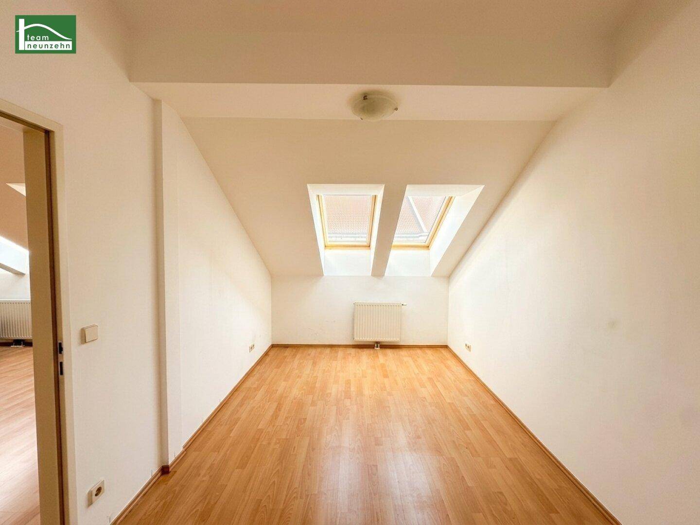 Helles Zimmer im Dachgeschoss mit Holzboden und zwei Dachfenstern.