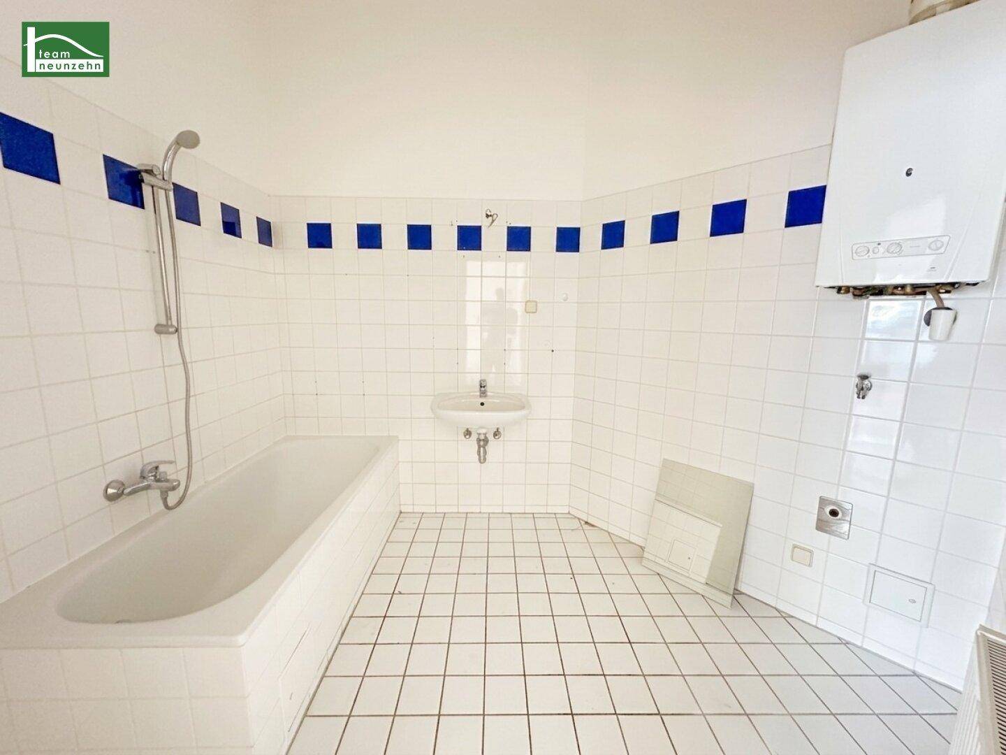 Badezimmer mit Badewanne, Waschbecken und blauen Akzentfliesen an den Wänden.