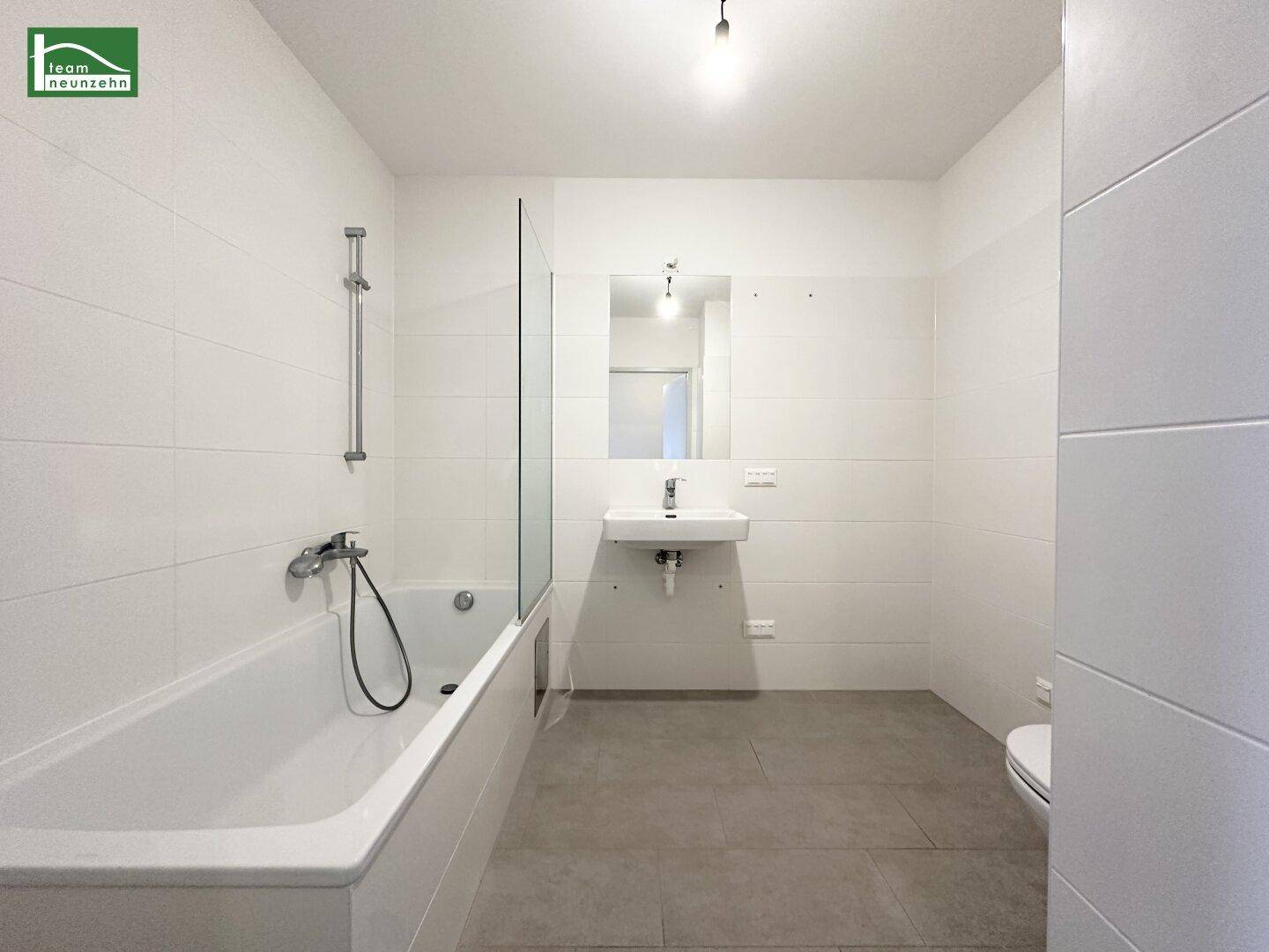 Modernes Badezimmer mit Badewanne, Duschwand und hellen Fliesen.