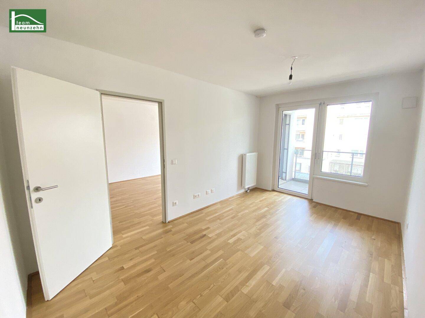 Helles Zimmer mit Holzboden und Zugang zu einem französischen Balkon.