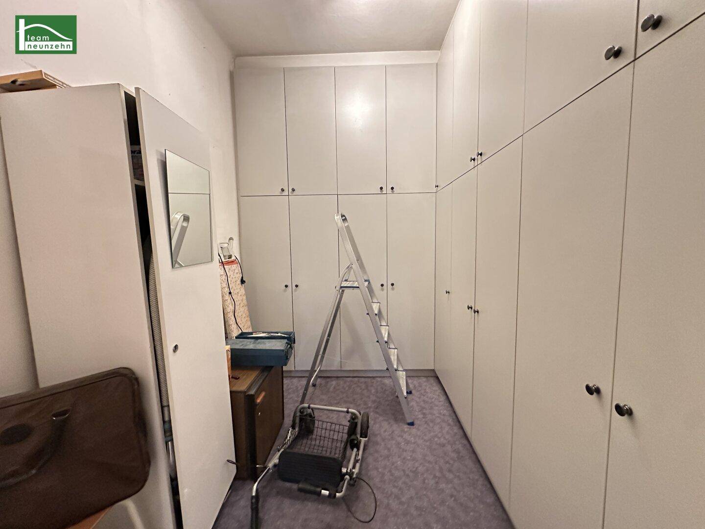 Langer Raum mit vielen Einbauschränken und Teppichboden, ideal als Ankleide oder Abstellraum.