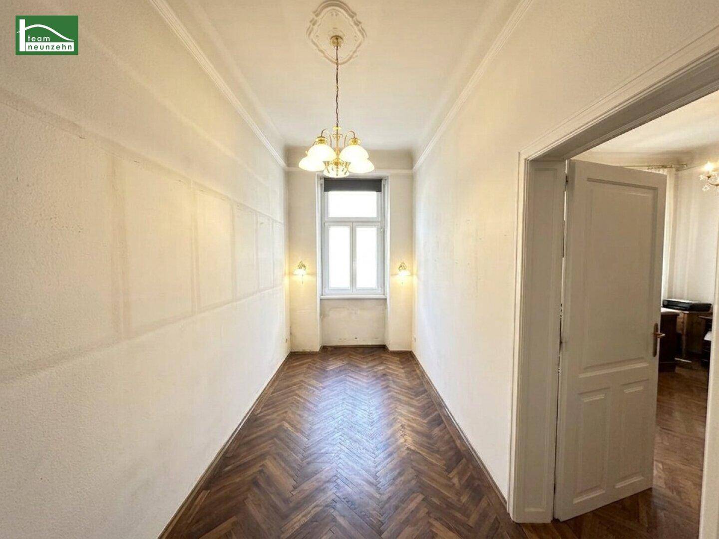 Schmaler Raum mit Fischgrätparkett und einem Fenster, der als Flur oder Durchgang dient.