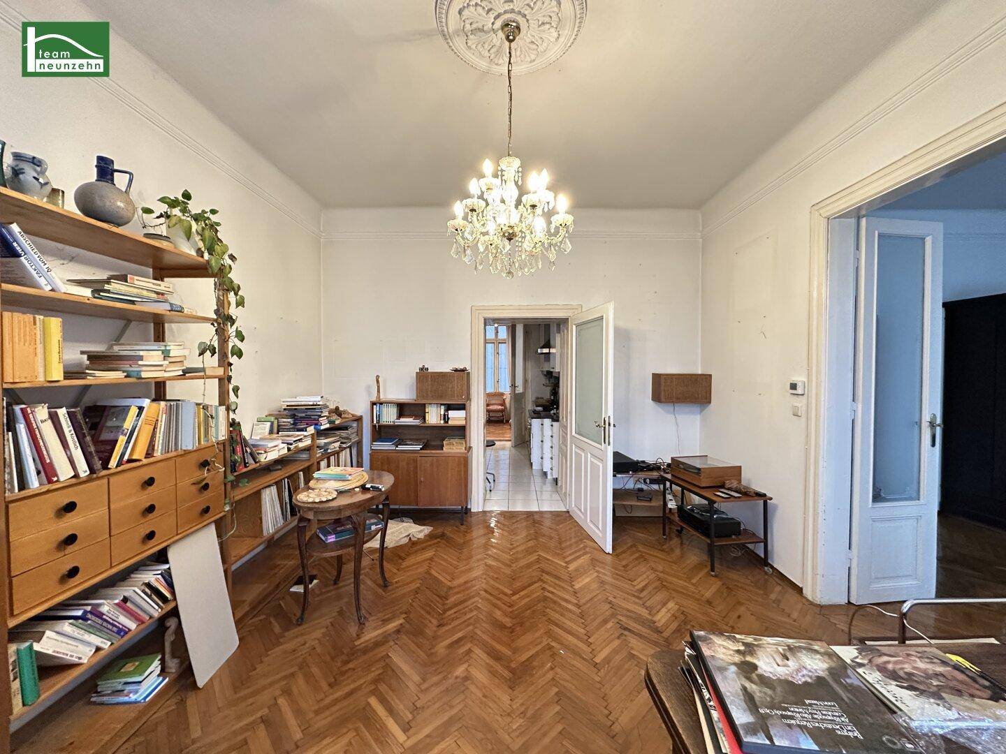 Helles Wohnzimmer mit klassischem Fischgrätparkett, Kronleuchter und Blick in den Flur.