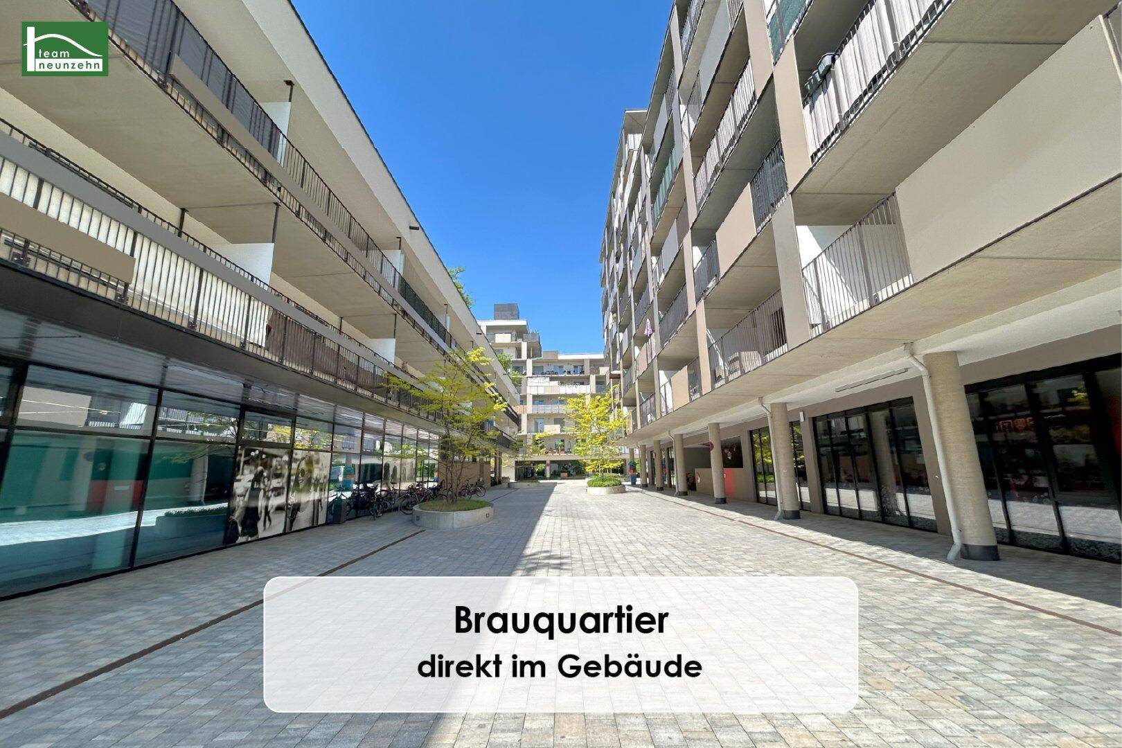 Moderne Wohnanlage mit Geschäften im Erdgeschoss und einem hellen, gepflasterten Innenhof.