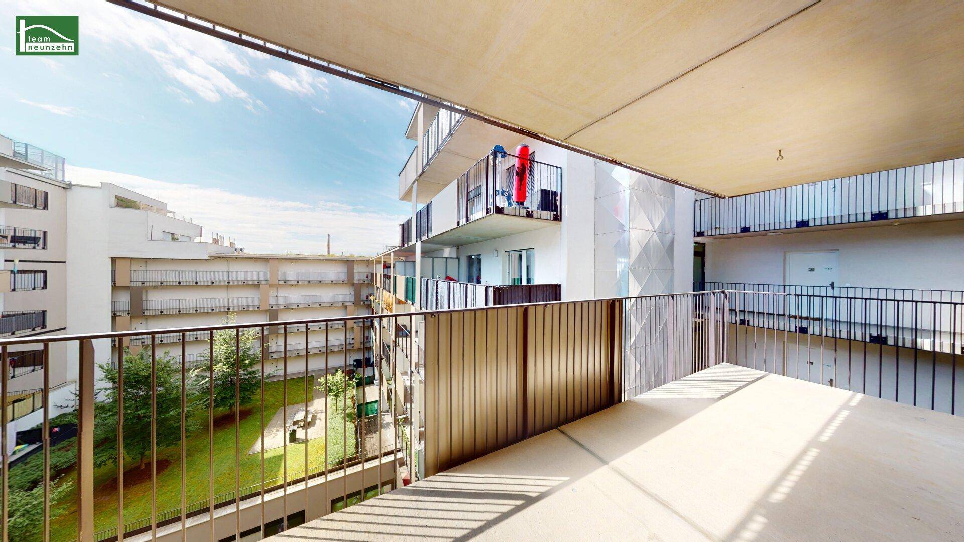Geräumiger Balkon mit Metallgeländer und Blick auf den grünen Innenhof der Wohnanlage.