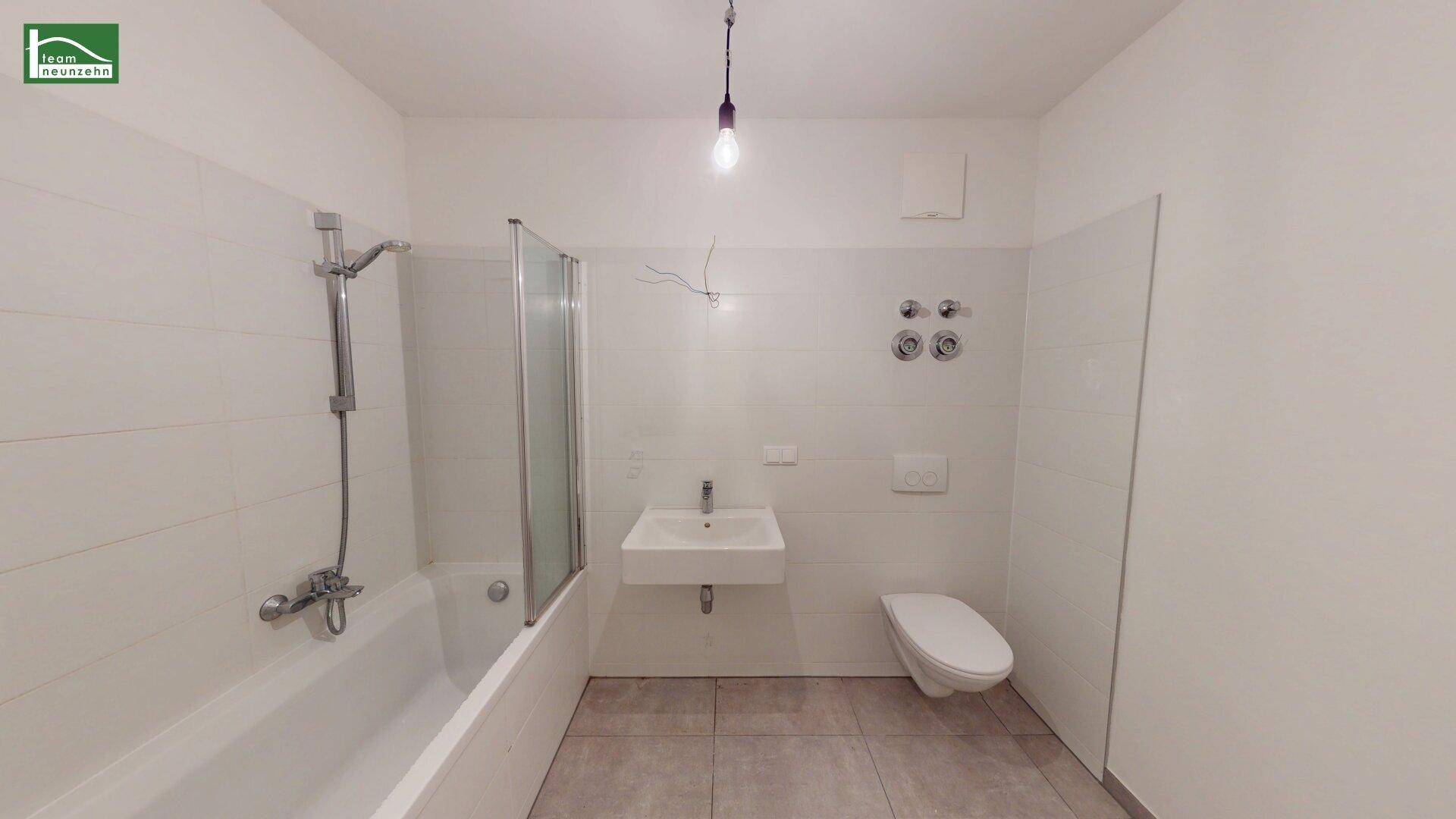 Modernes Badezimmer mit weißen Fliesen, Badewanne mit Duschfunktion und wandhängendem WC.