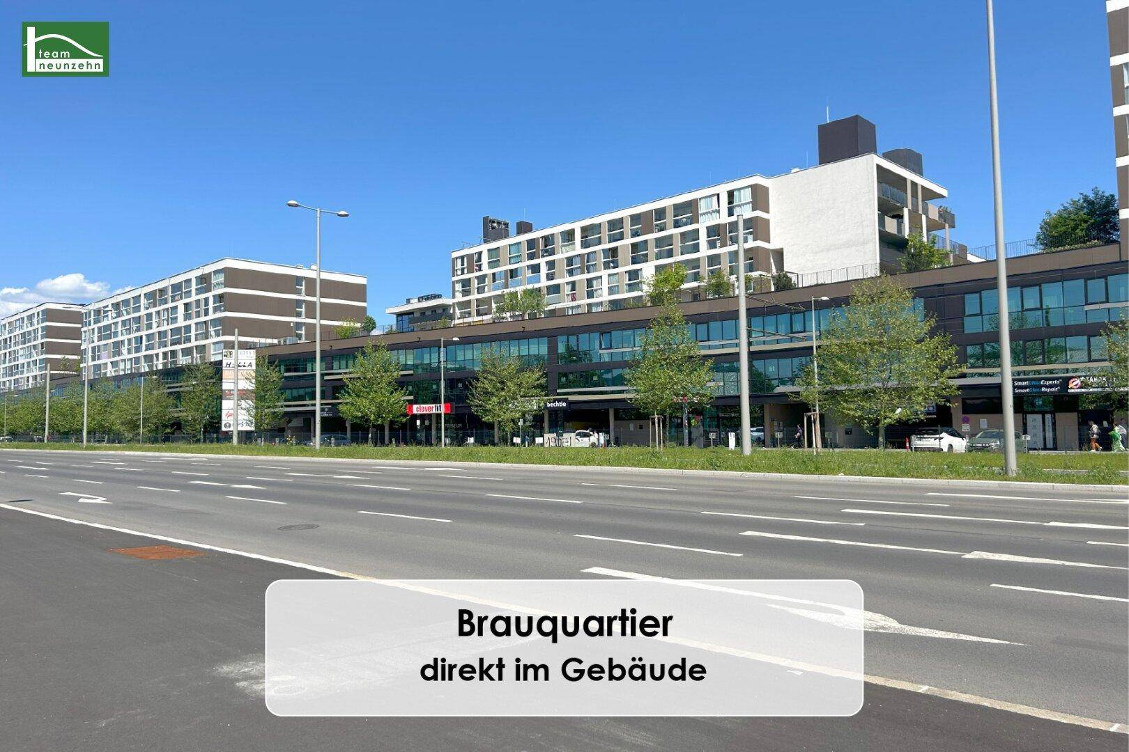 Weitläufige Ansicht des modernen Brauquartiers mit Gebäuden, Straße und viel Grün.
