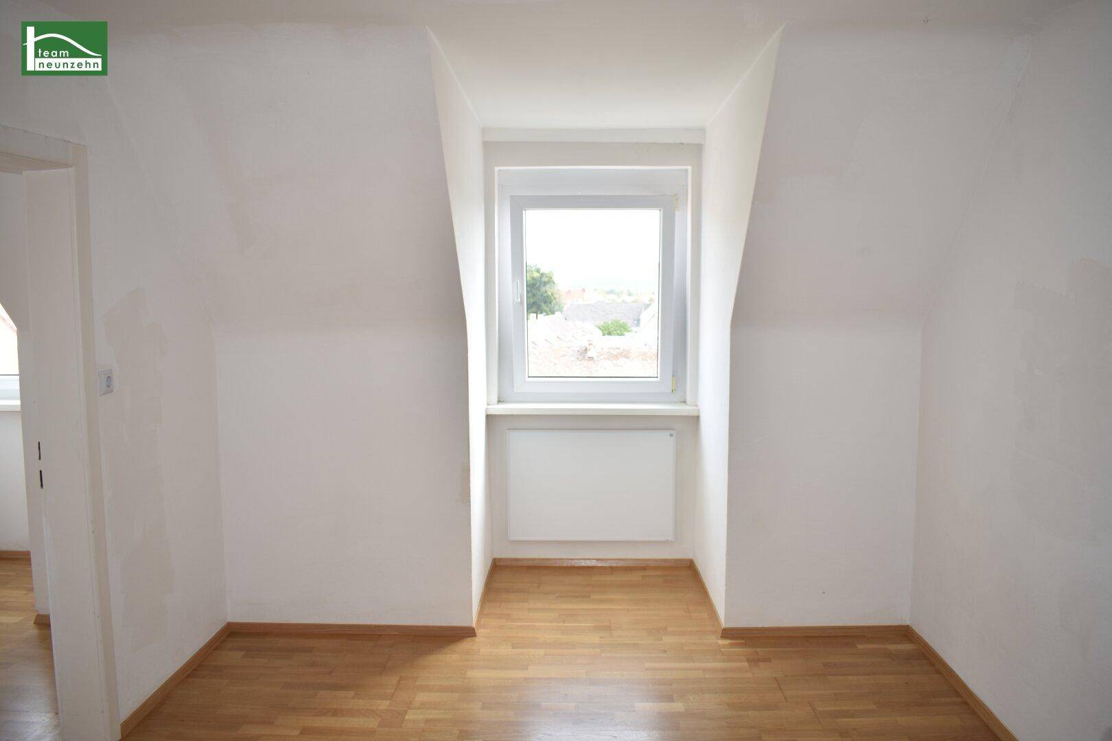 Leeres Zimmer im Dachgeschoss mit Dachschrägen, Parkettboden und einem Fenster für Tageslicht.