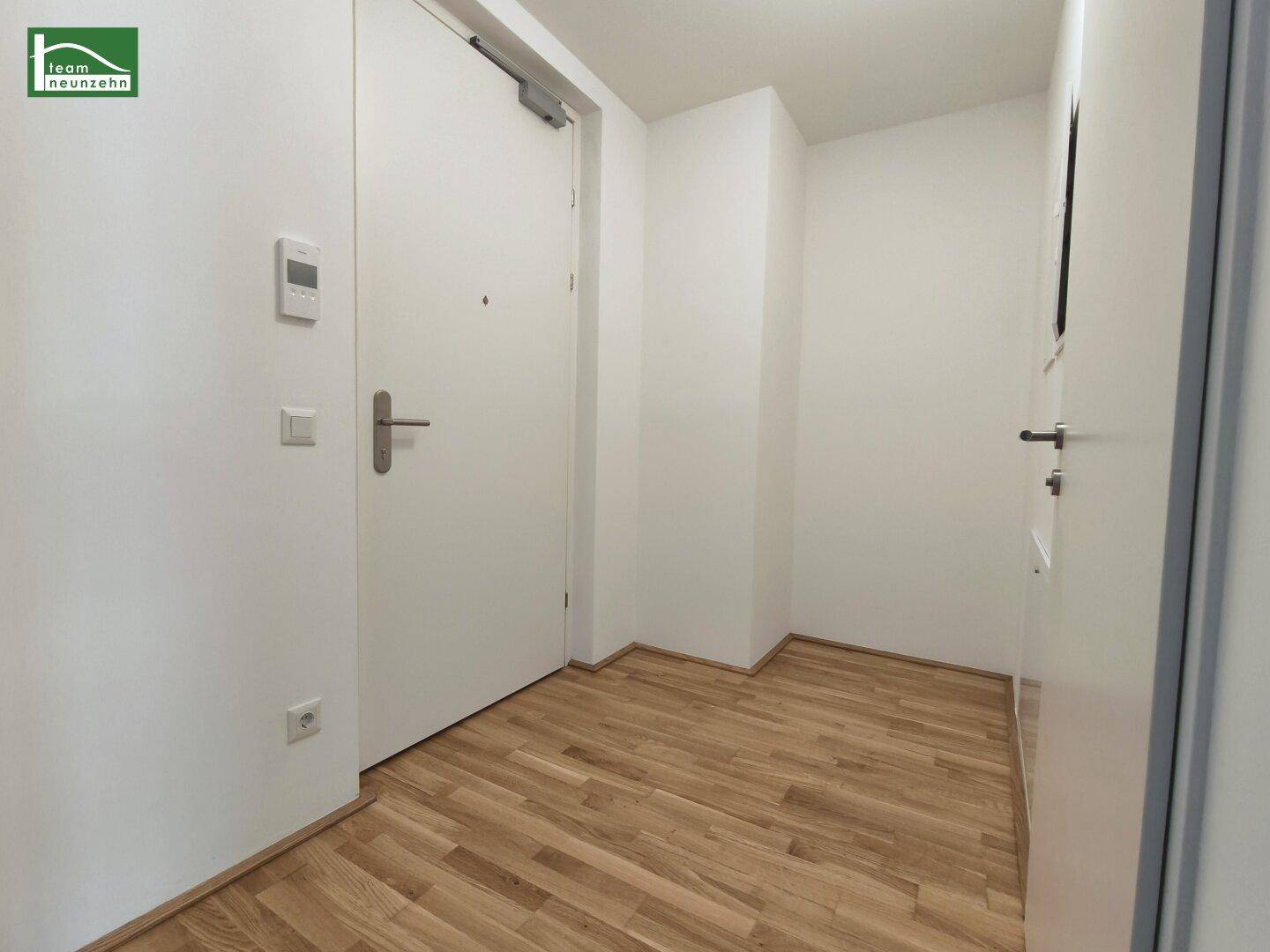 Heller Eingangsbereich mit Holzboden und weißer Eingangstür, die in die Wohnung führt.