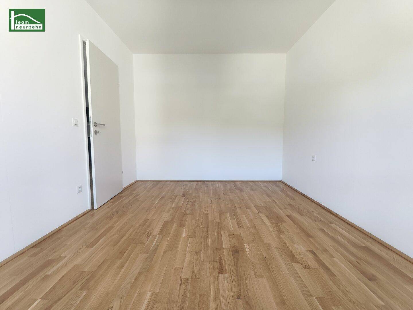 Leeres Zimmer mit Holzboden und weiß gestrichenen Wänden, bereit zur individuellen Gestaltung.