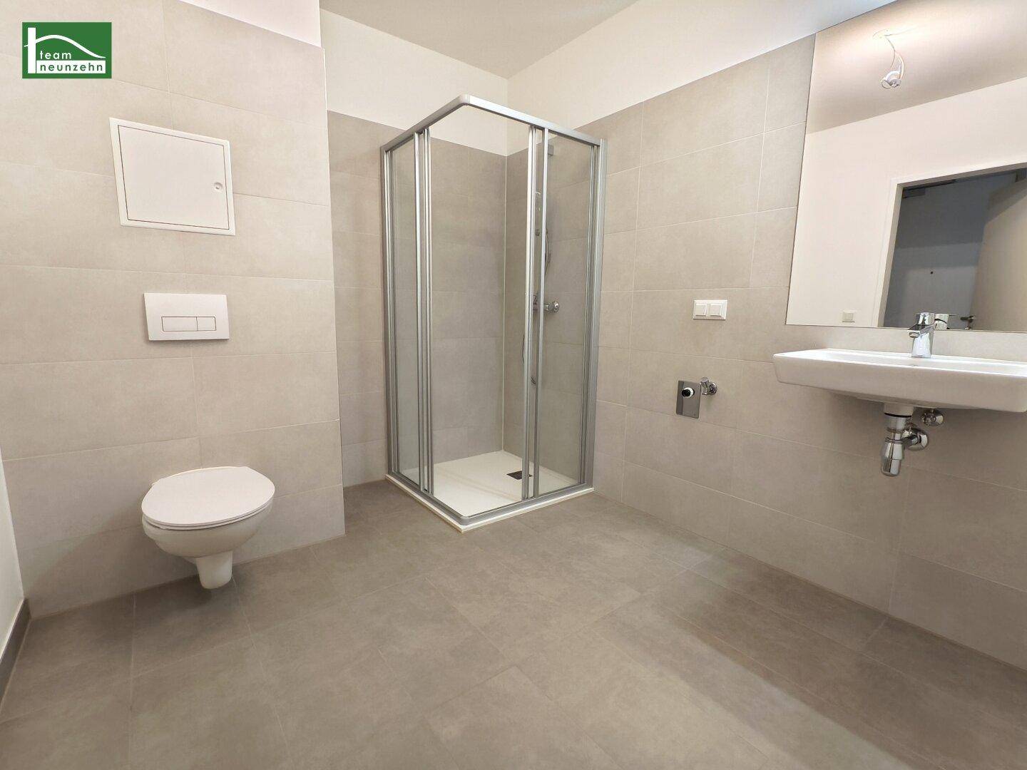 Modernes Badezimmer mit Duschkabine, WC, Waschbecken und hellen Fliesen.