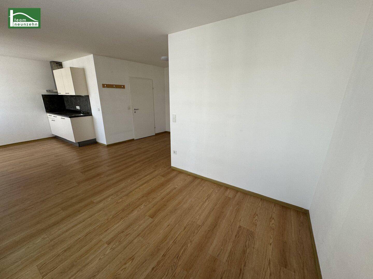 Geräumiger, heller Raum mit Laminatboden und einer kleinen Küchenzeile im Hintergrund.