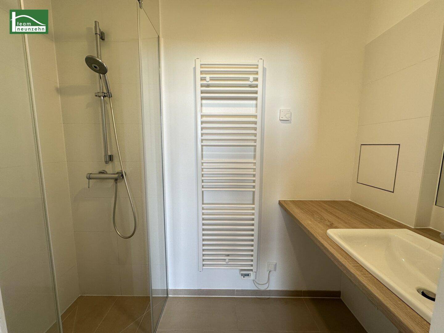Modernes Badezimmer mit ebenerdiger Dusche, Einzelwaschbecken und beheiztem Handtuchhalter.