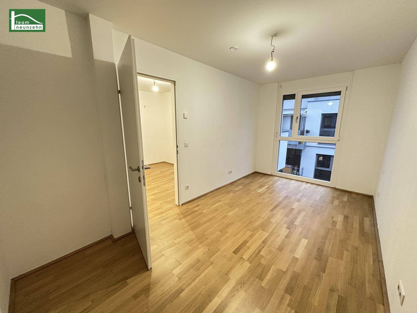 Leeres Zimmer mit hellem Holzboden und großem Fenster, bereit zur individuellen Gestaltung.