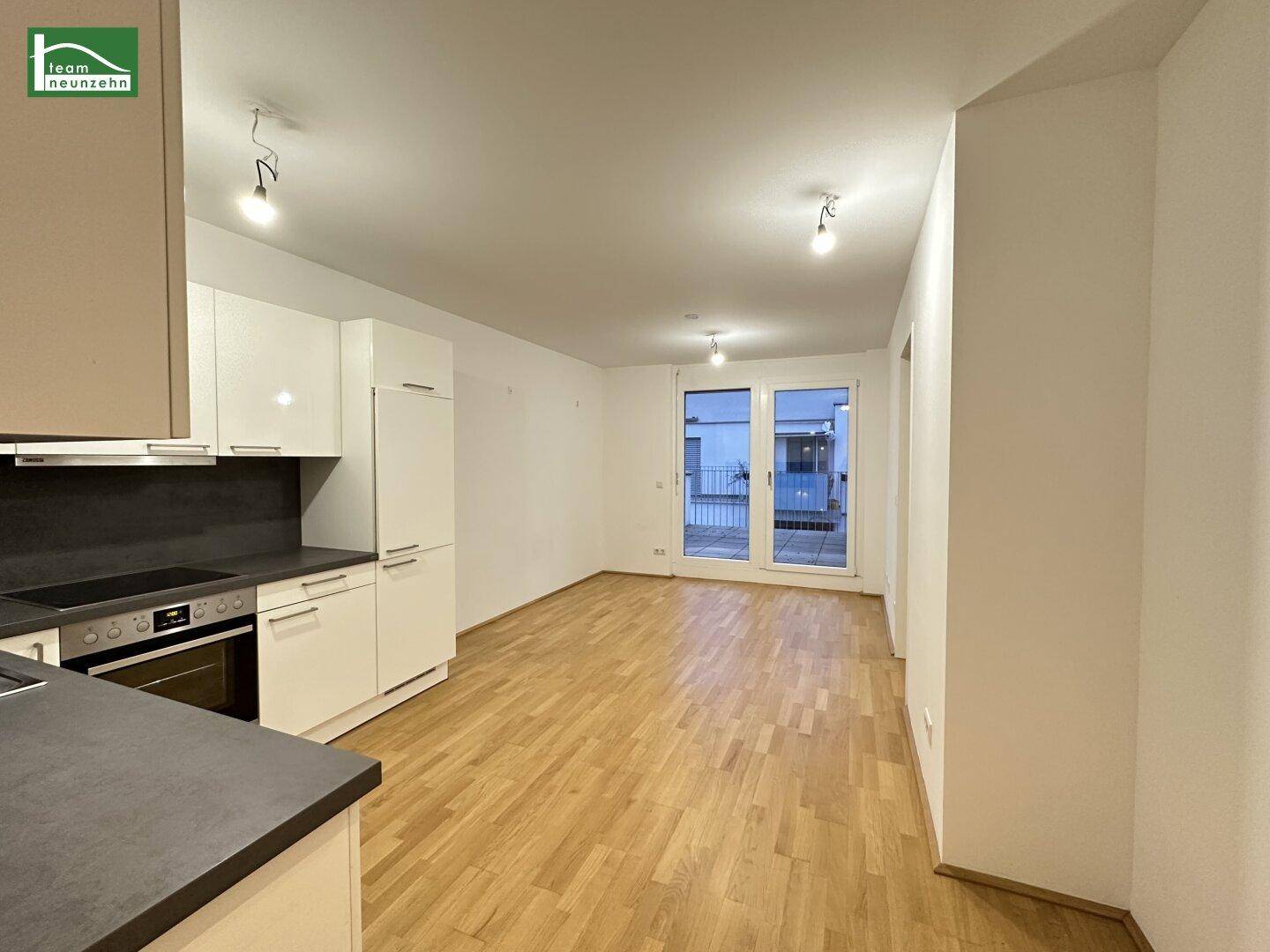 Offener Wohnbereich mit integrierter Küche, Holzboden und Zugang zu einem Balkon.