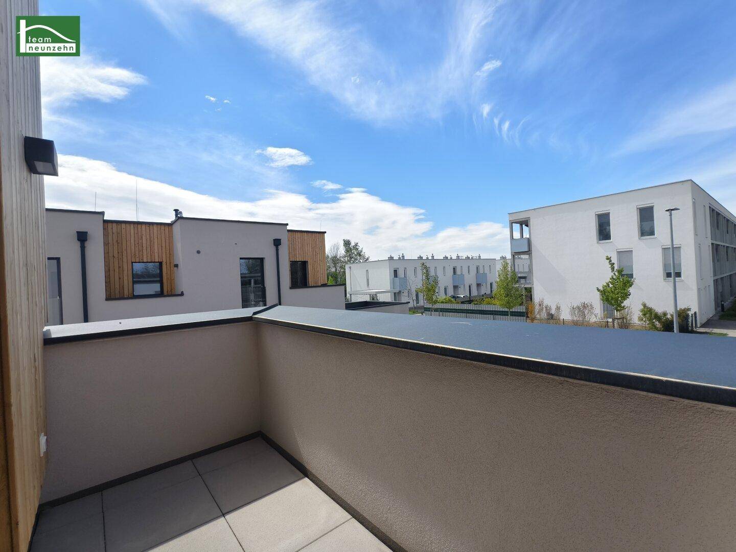 Kleiner Balkon mit Blick auf die umliegenden Neubauten und den blauen Himmel.