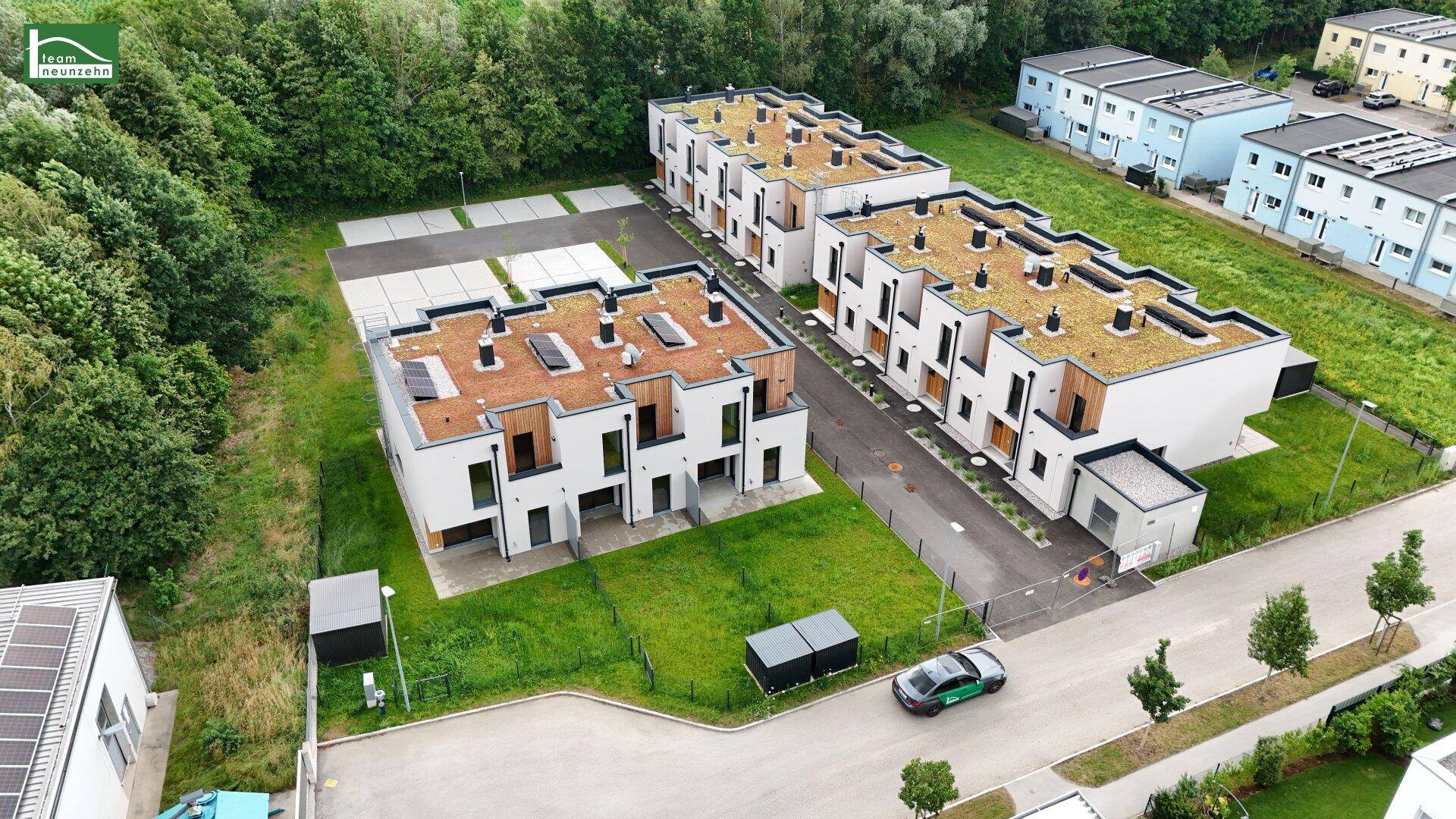 Luftaufnahme einer Wohnanlage mit mehreren Reihenhäusern, Gründächern und angrenzenden Grünflächen.