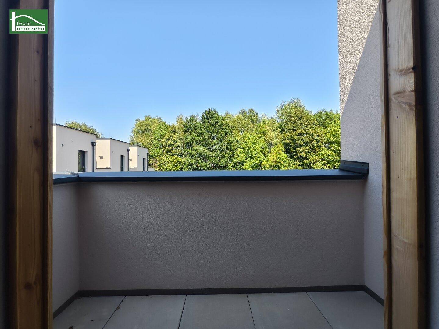 Balkon mit Fliesenboden und Blick auf grüne Bäume und die umliegende Bebauung.