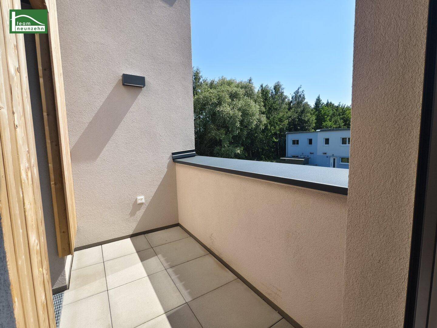 Kleiner Balkon mit Fliesenboden und Blick ins Grüne sowie auf benachbarte Gebäude.
