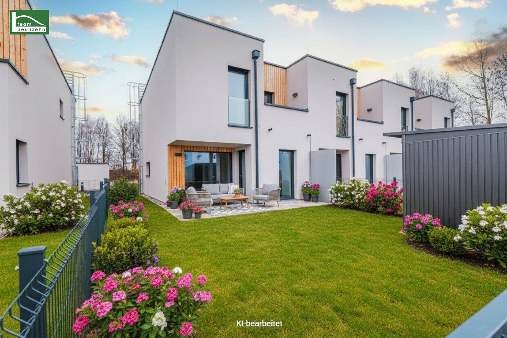 Moderne Reihenhäuser mit gepflegtem Rasen, blühenden Blumenbeeten und einer möblierten Terrasse.