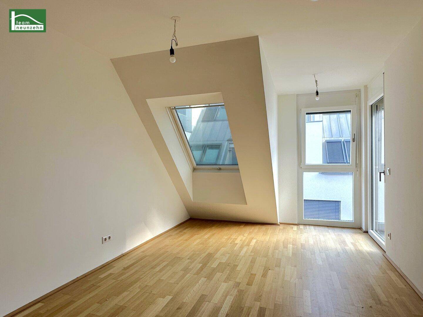 Unmöbliertes Wohnzimmer mit hellem Parkettboden, Dachschräge und Zugang zum Außenbereich.