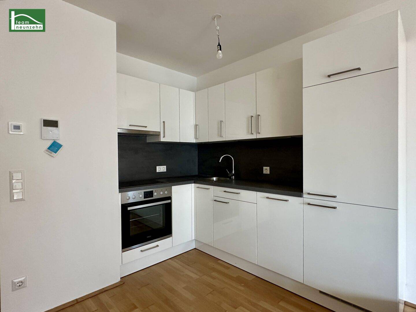Moderne Einbauküche mit weißen Hochglanzfronten, dunkler Arbeitsplatte und integriertem Backofen.
