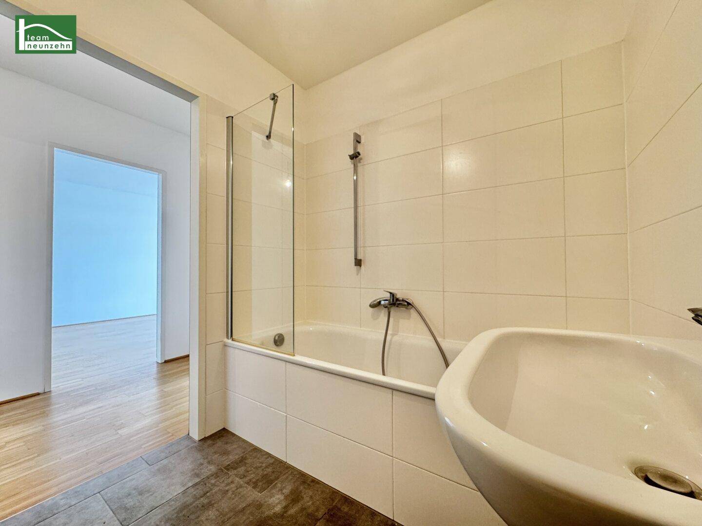 Badezimmer mit Badewanne, Duschabtrennung und einem einzelnen Waschbecken, hell gefliest.
