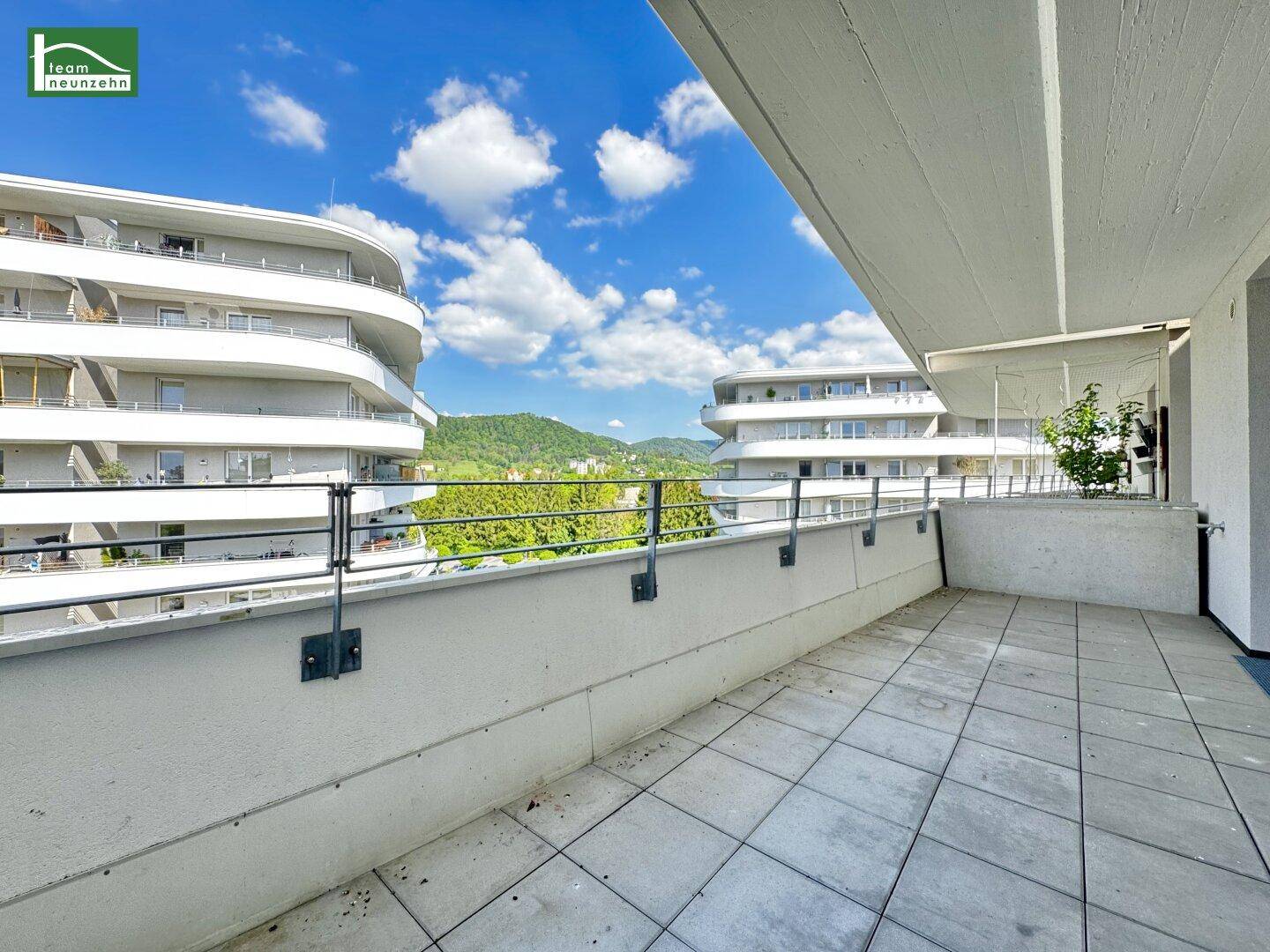 Großer Balkon mit Fliesenboden und weitem Blick auf die modernen Gebäude und grüne Hügel.